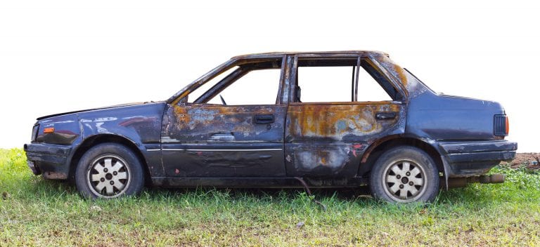 Isolate old blue sedan, which was burnt to the devastated parked on the grass.
